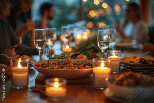 A warm, intimate dinner setting with friends featuring a salad bowl and wineglasses illuminated by candlelight © punniix