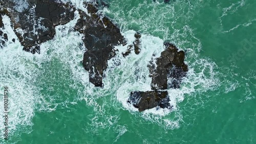 Drone top down ascend above ocean waves pulsing across rocks breaking surface photo