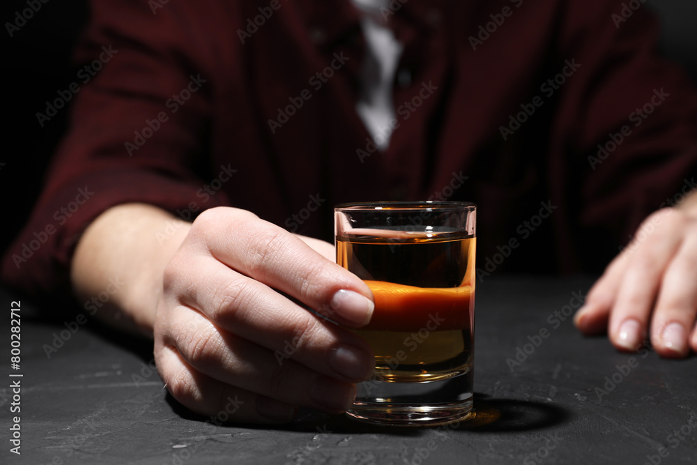 Alcohol addiction. Woman with glass of whiskey at dark textured table, selective focus
