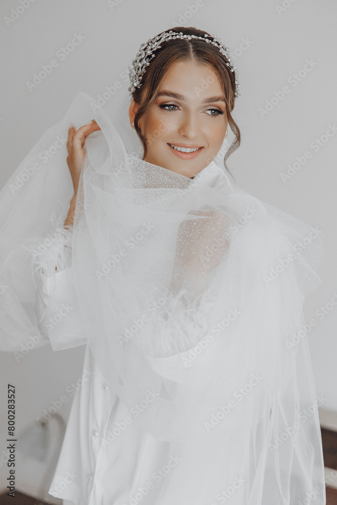A woman is wearing a white dress and a veil. She is smiling and holding a white cloth