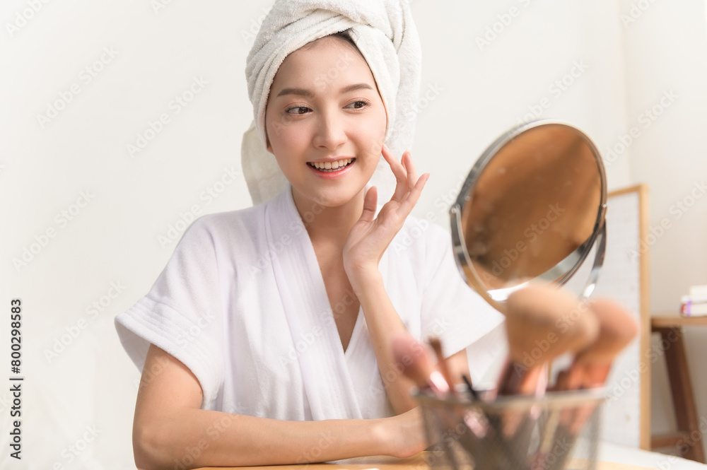 Close up portrait photo of young beautiful Asian woman taking care of her facial skin after apply face skin care cosmetic lotion moisturizer product and checking in mirror at home. Beauty care concept Close up portrait photo of young beautiful Asian woman taking care of her facial skin after apply face skin care cosmetic lotion moisturizer product and checking in mirror at home. Beauty care concept