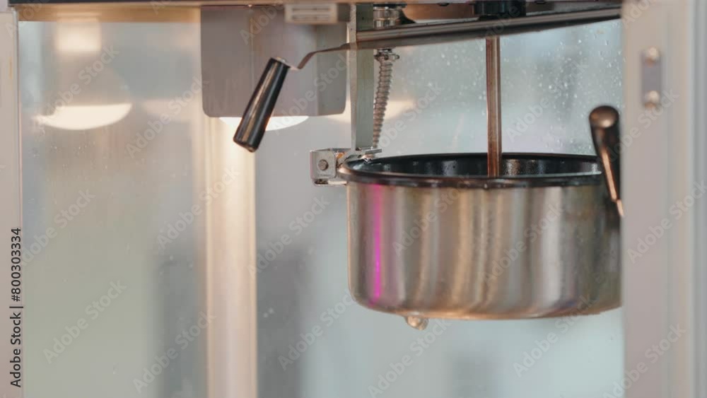 Close-up of a hot, steaming popcorn pan inside a popcorn machine, with a handle in view
