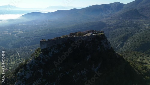 Aerial panoramic orbit around Karytaina Castle with misty low clouds in valley below on sunny day photo