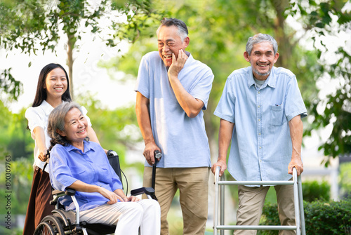 group of senior people with rehabilitation equipment enjoy talking together,a smiling teenager pushing a wheelchair for grandma,elderly asian friends spend their time in the park © Verin