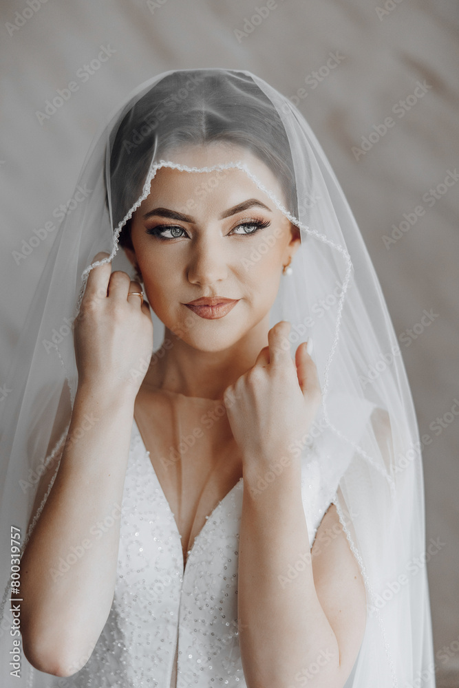 Fototapeta premium A woman is wearing a veil and is smiling. She is wearing a white dress and has her hands on her head