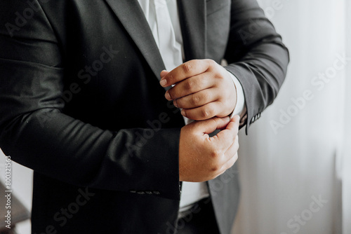 A man in a black suit is getting ready to dress up. He is adjusting his tie and shirt, and his hands are clasped together. Concept of formality and professionalism
