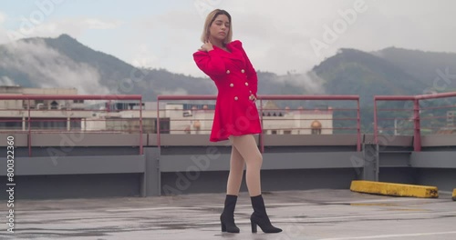 Amidst the urban sprawl, a young girl of Hispanic heritage stands elegantly in her short red dress atop a rooftop. photo