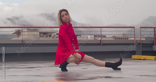On the urban rooftop, a youthful Hispanic girl stands gracefully in her short crimson attire. photo