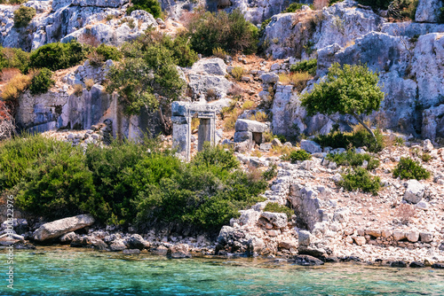 Time-worn Lycian ruins stand among wild shrubs on Kekova Island, vibrant colors. Famous boat tour from Demre, Antalya, Turkiye (Turkey) © Elena