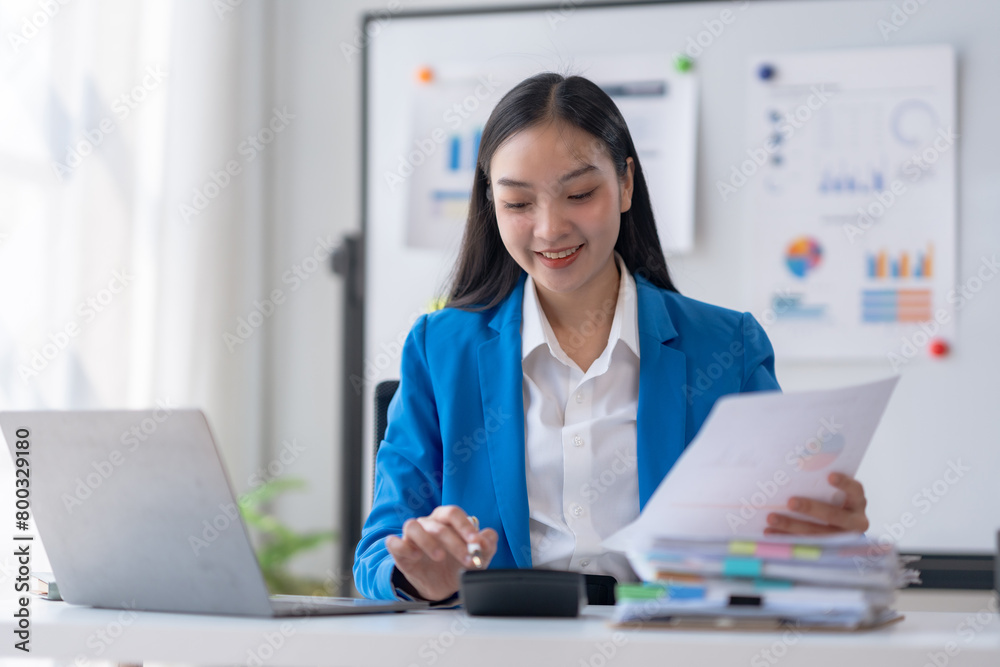 Young Asian businesswoman using a calculator to calculate business principles. Accounting statistics concept at the office. Young Asian businesswoman using a calculator to calculate business principles. Accounting statistics concept at the office.