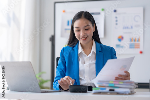 Young Asian businesswoman using a calculator to calculate business principles. Accounting statistics concept at the office.