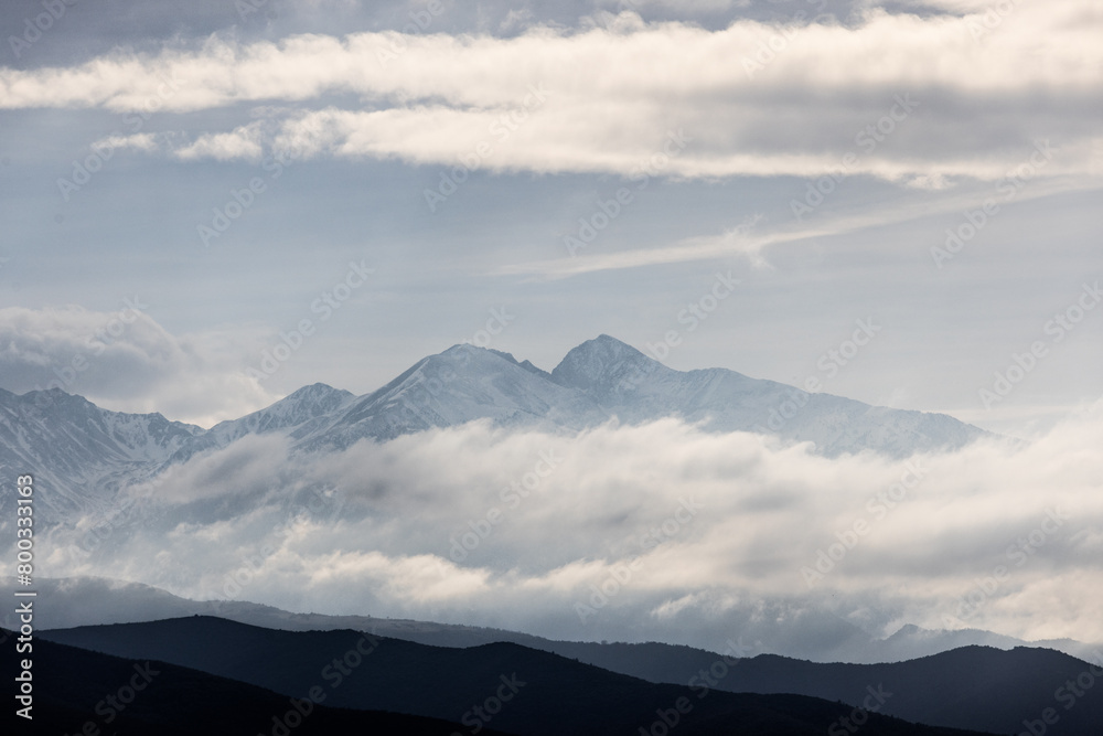 The sky is cloudy and the mountains are covered in snow. The mountains are tall and majestic, and the clouds add a sense of depth and mystery to the scene