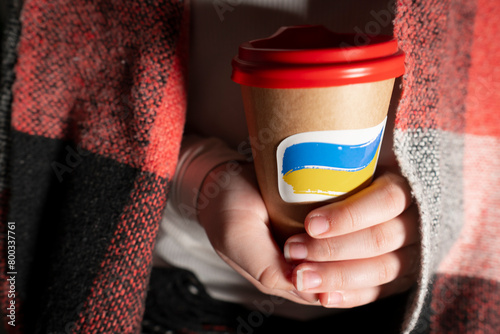 Blackout. A cardboard cup of coffee with a sticker in the shape of the national flag of Ukraine in hands close-up