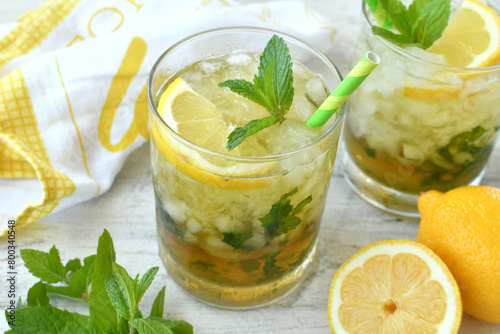 Cocktail or lemonade drink with lemon, muddled mint garnish, green straws, lemon slices