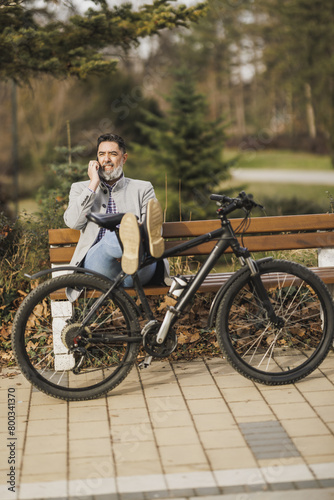 Man Sitting on Bench Next to Bike and Using Smart Phone