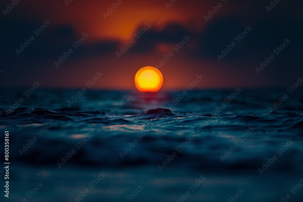 Out of focus sun setting over the ocean glowing orange with dark blue background