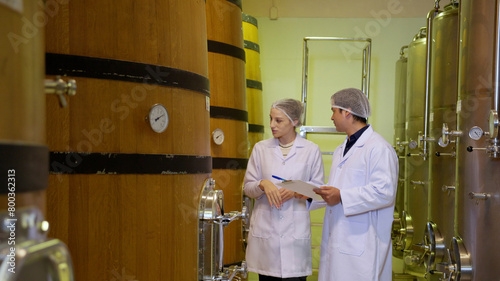 Winemaker team checking and examining producing wine at winery in factory, inspector checking quality and fermenting wine storage in tank or barrel at room, industrial and manufacture concept.