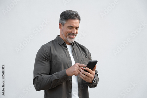 Smiling hispanic business man using smartphone mobile phone device for online financial bank transactions. 40s freelancer entrepreneur in casual shirt holding cellphone isolated on white background