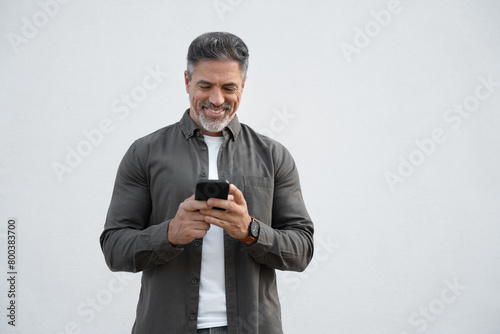 Smiling hispanic business man using smartphone mobile phone device for online financial bank transactions. 40s freelancer entrepreneur in casual shirt holding cellphone isolated on white background