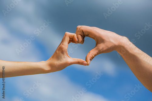 Girl and man hands in heart form over blue sky background. Love, friendship concept. Girl and male hand in heart form love blue sky. Female and man hands in form of heart against the sky © Yevhen