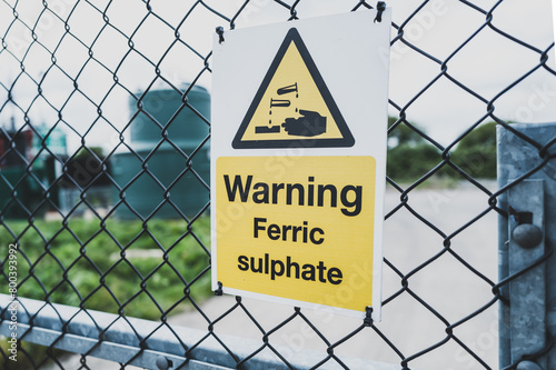 Shallow focus of a Warning sign displaying that Ferric Sulphate is used at this sewage treatment plant in the UK. The corrosive effects are seen in the warming triangle.