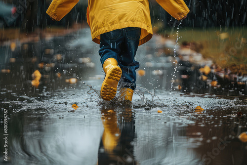 Close up Child in rubber boots and yellow raincoat jumping in puddle