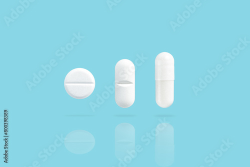 Various white medicine pills levitate over a blue background. Shadow and reflection from drugs