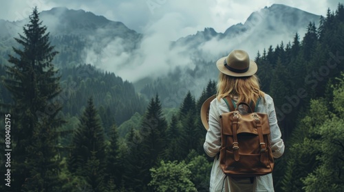 Woman traveler with backpack holding hat and looking at amazing mountains and forest, wanderlust travel concept, space for text, atmospheric epic moment © Elchin Abilov
