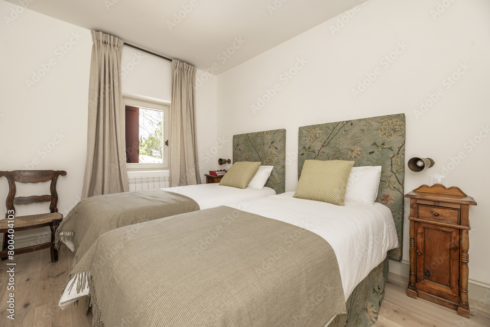 Detail of a bedroom with twin beds with headboards upholstered in printed fabric and vintage wooden nightstands.