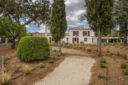 a dirt road in the middle of newly planted gardens with trees and a country house photo