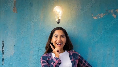 Illuminated light bulb above the head of a young woman, the concept of having an idea of a surprised girl with eureka on an old blue wall 