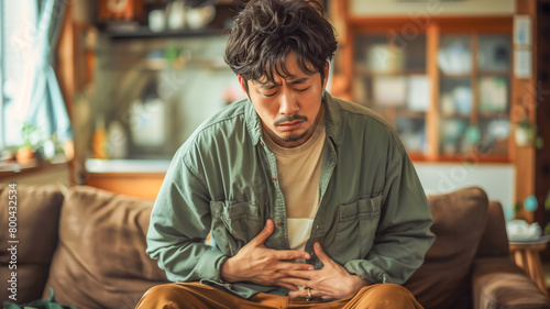  Asian man clutching his stomach have stomachache sitting on sofa , diarrhea problem concept photo