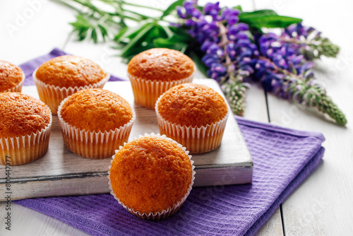 Freshly baked muffins and purple lupins on white wooden background. Homemade baking, preparing sweet dessert. Summer recipe. © Galina Atroshchenko