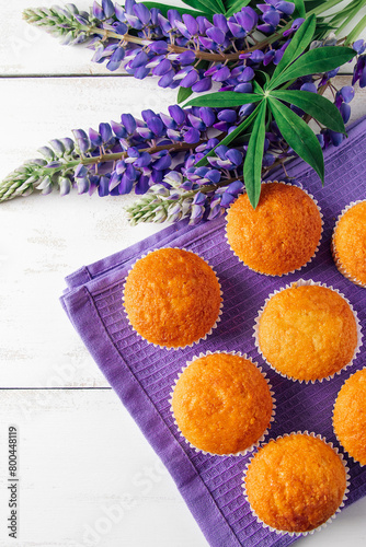 Freshly baked muffins and purple lupins on white wooden background. Homemade baking, preparing sweet dessert. Summer recipe. Vertical photo. © Galina Atroshchenko