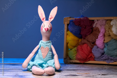 Textile handmade toy of pink bunny girl against blue background and wooden box with tissues