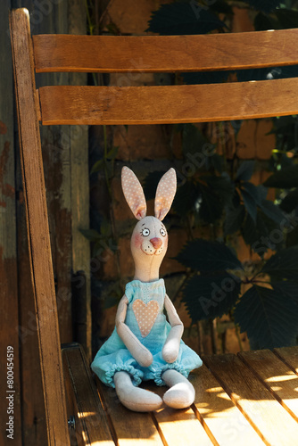 Textile handmade toy of pink bunny girl sitting on a chair