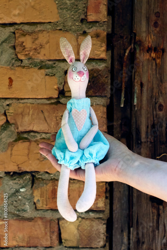 Textile handmade toy of pink bunny girl sitting on woman hand