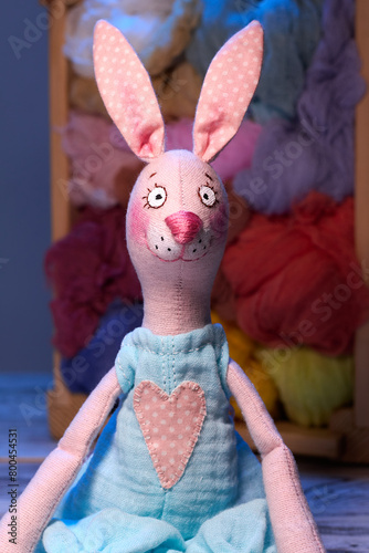 Textile handmade toy of pink bunny girl against blue background and wooden box with tissues