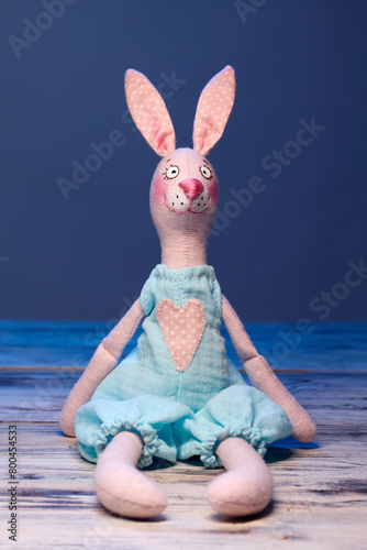 Textile handmade toy of pink bunny girl against blue background