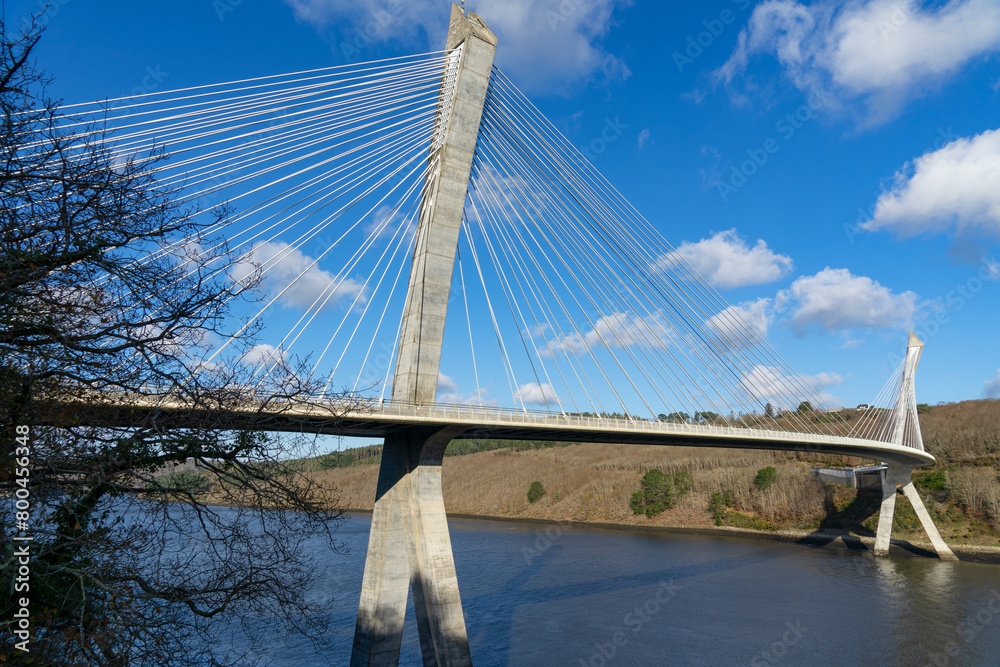 Fototapeta premium Sous un ciel bleu éclatant, le pont de Térénez, pont à haubans courbé au-dessus de l'Aulne, offre une vue emblématique à l'entrée de la presqu'île de Crozon, dans le Finistère, en Bretagne.