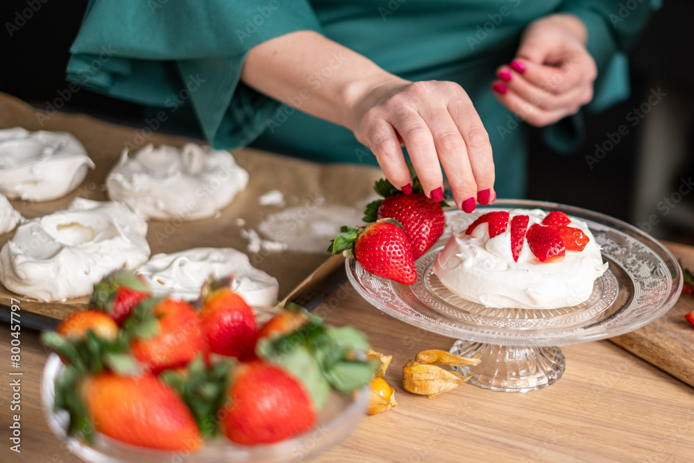 A chef in a green apron assembles strawberry pavlovas in a bright kitchen, with more desserts in soft focus behind. Ideal for culinary websites and dessert blogs. A chef in a green apron assembles strawberry pavlovas in a bright kitchen, with more desserts in soft focus behind. Ideal for culinary websites and dessert blogs.