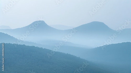   A view of a mountain range shrouded in fog, with distant mountains and trees in the foreground © Viktor