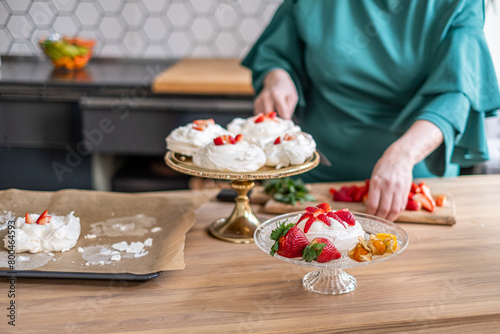 Person preparing pavlovas with fresh strawberries, kitchen setting. Ideal for a cooking tutorial.