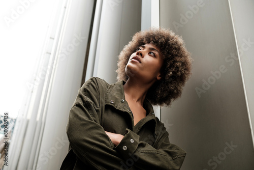 Curly female model leaning on metallic wall and looking up.