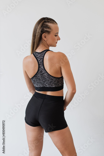 Focused young woman in sports attire stands on yoga mat, preparing for workout. Her attire suggests readiness for physical activity, combined with a subtle expression of determination and wellness.