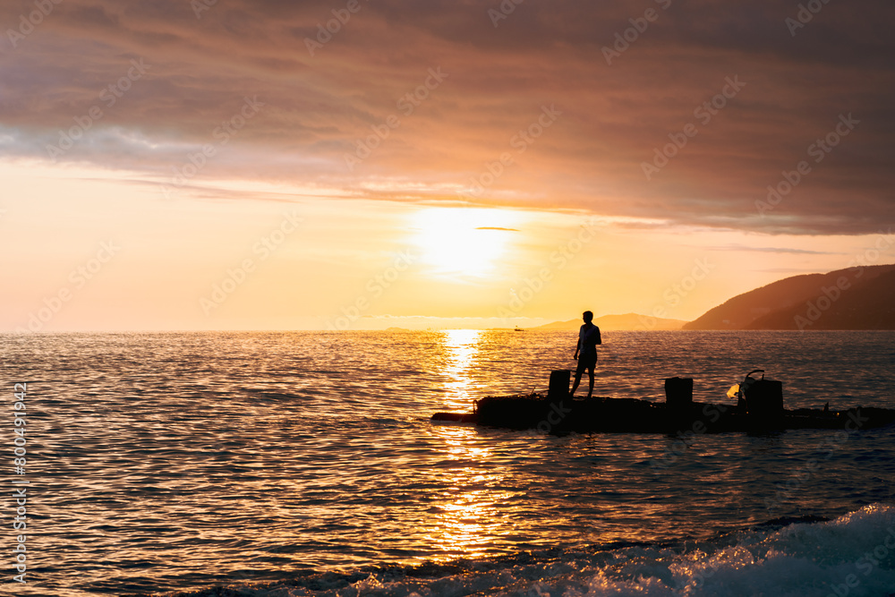 A man is fishing in the ocean at sunset