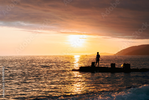 A man is fishing in the ocean at sunset