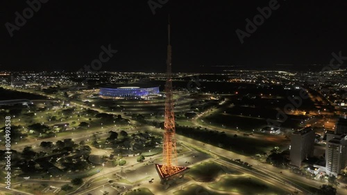 Drone orbits around orange TV Tower as it changes to red, with blue Arena BRB Mane Garrincha in background and lit up Ferris Wheel in Castelinho do Parque da Cidade in Brasilia, Brazil photo