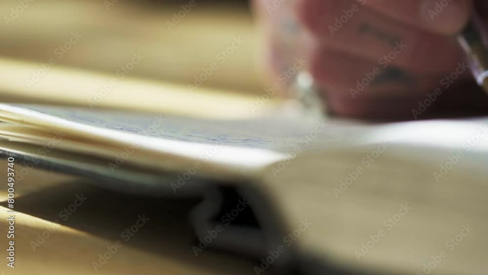 Caucasian tattooed artist writer right hand holding ink pen writing new idea on paper notebook journal. Extreme close up