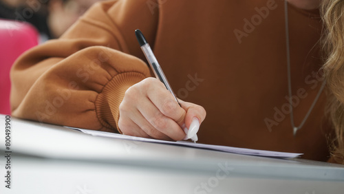 A girl is writing a dictation, preparing an answer in an exam, or filling out documents in the classroom, sitting at a desk .Photo. Selective focus. Close-up © slexp880